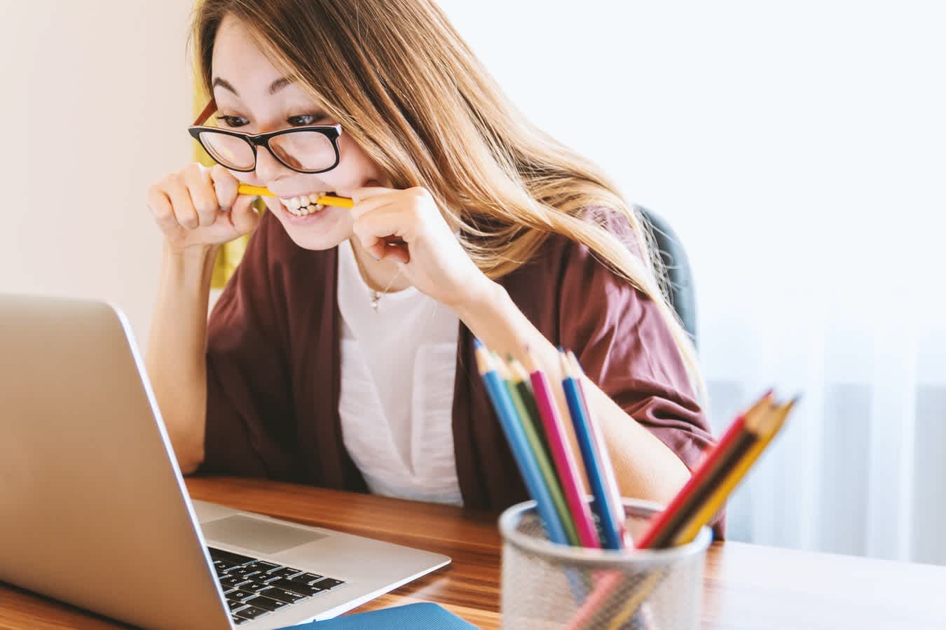 Woman biting on yellow pencil looking at laptop