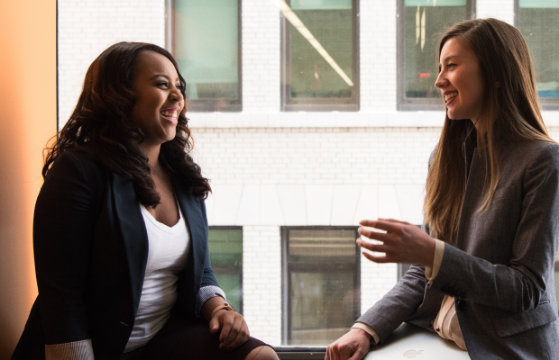 two women sitting on a window sill talking
