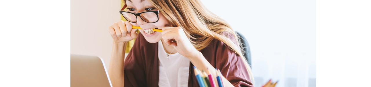 woman biting on pen in front of laptop