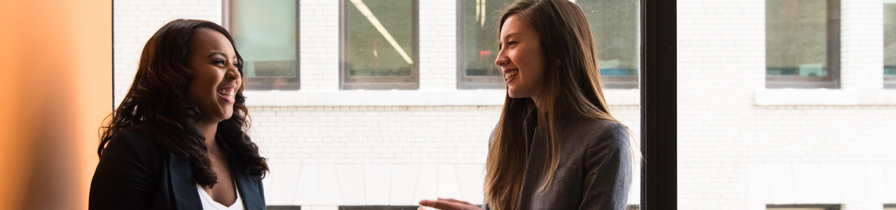 two women sitting on a window sill chatting 