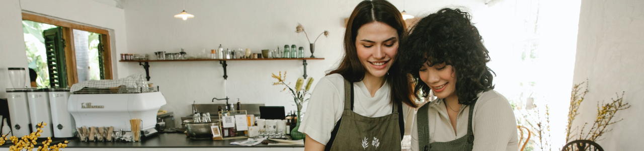 Two women working in a cafe serving cakes and smiling