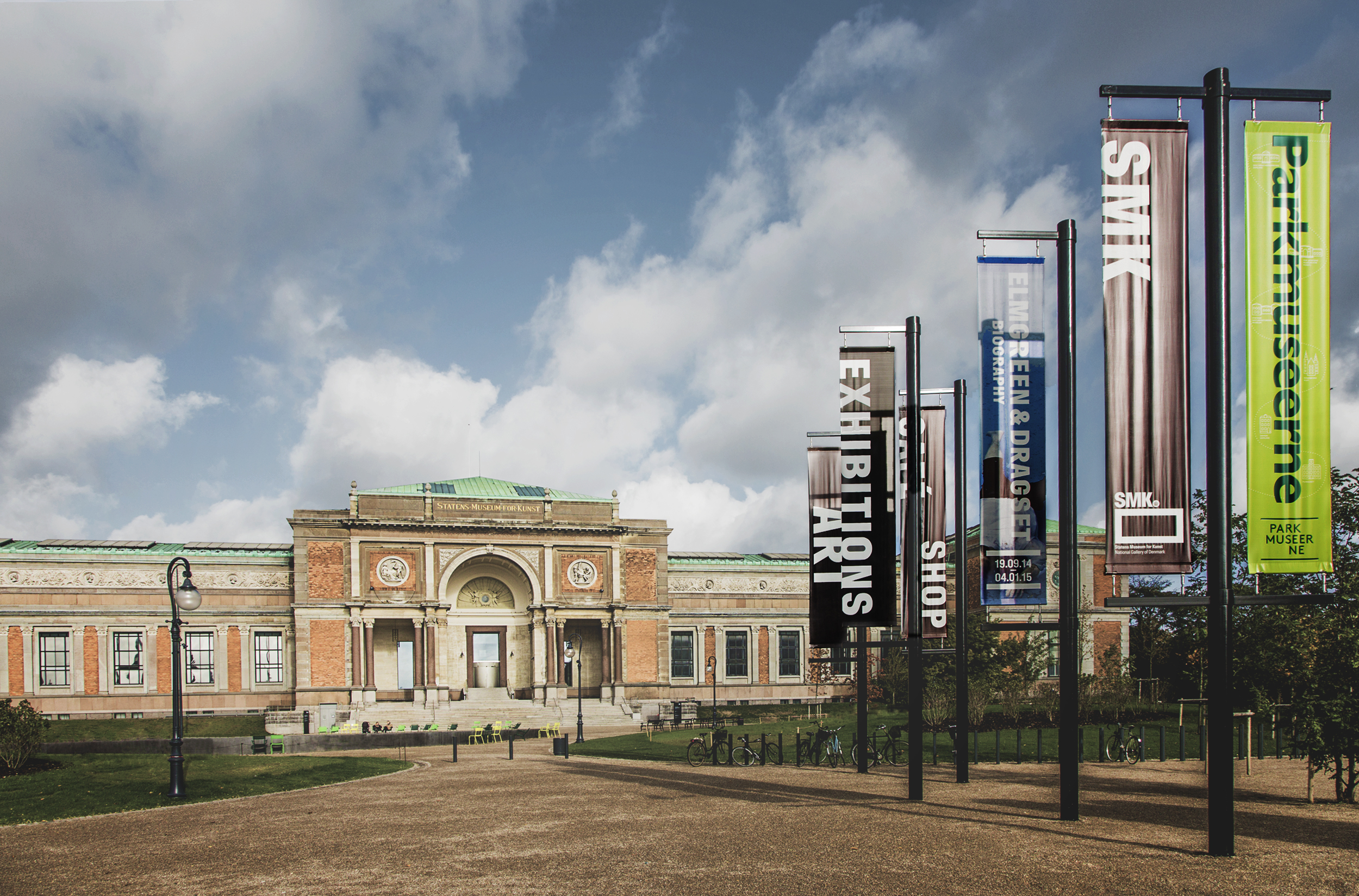 A photograph of the front of the SMK building, with a blue sky above and banners promotion exhibits. SMK - The National Gallery of Denmark by SMK Statens Museum for Kunst, CC BY 2.0
