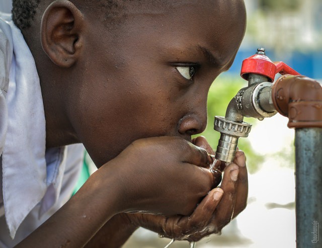 Young boy drinking water from spout with hands clasped together