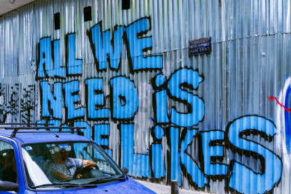 Blue graffiti on metal wall that reads 'All We Need is Likes' 