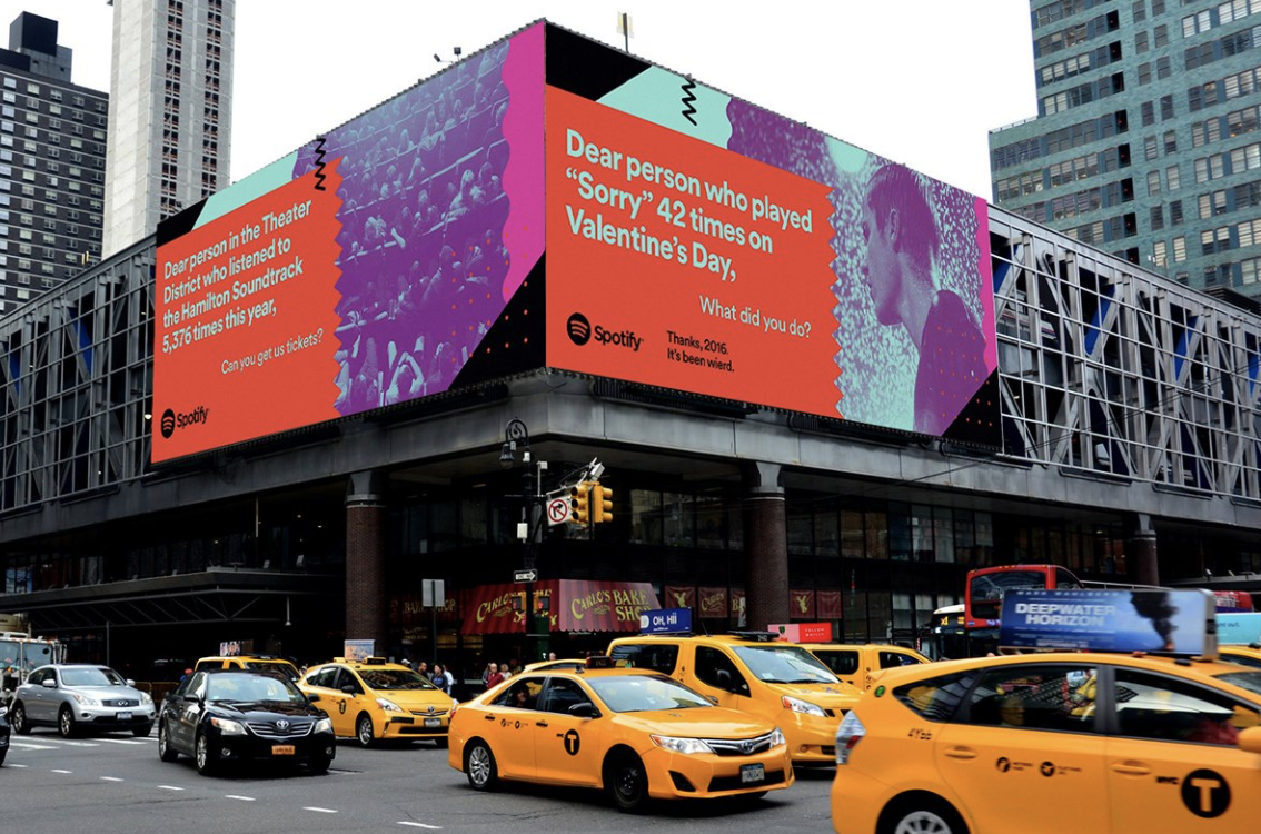 Image of two different Spotify billboards hanging on the side of a building in NYC with cabs driving across the street.