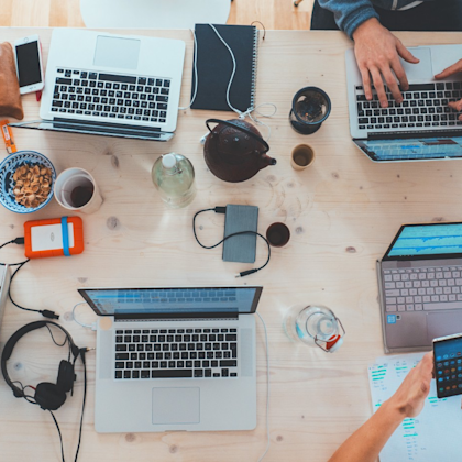 Laptops on table with hands, coffee, snacks, and headphones