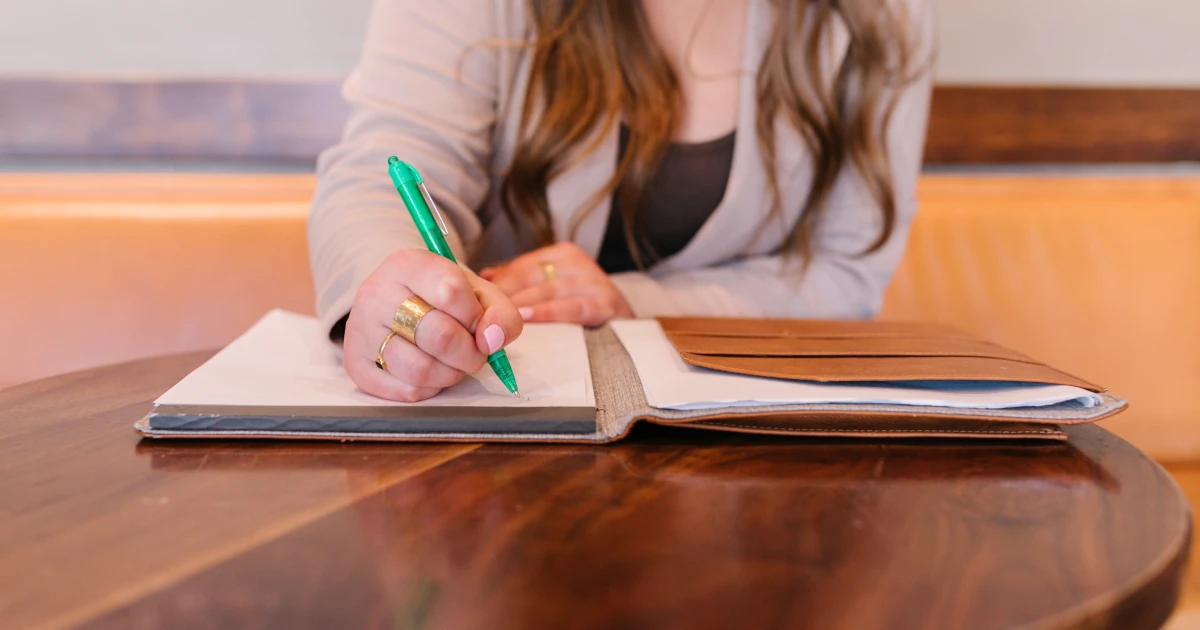 White woman sitting at brown circle table writing business plan