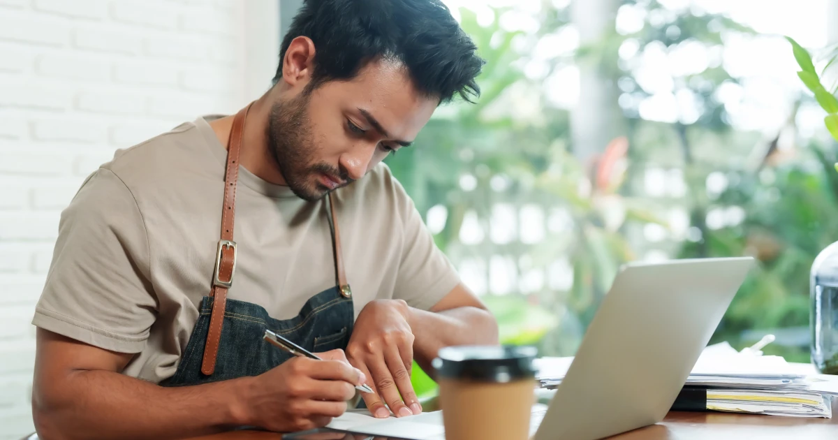 Indian man being barista and coffee shop owner sitting at desk