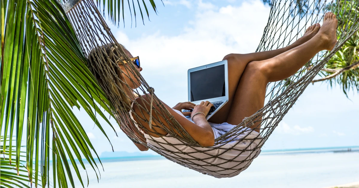 Woman laying in a hammock on a Hawaiian beach working on her laptop