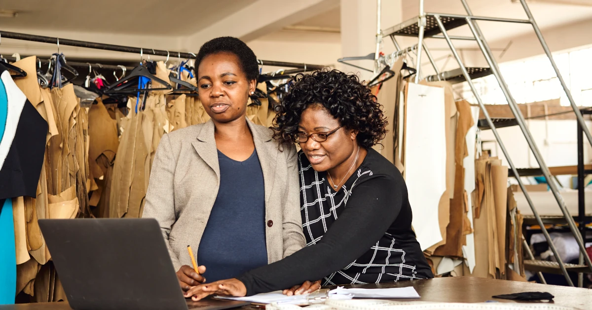 A black woman working with colleague processing paperwork with a laptop in textile factory