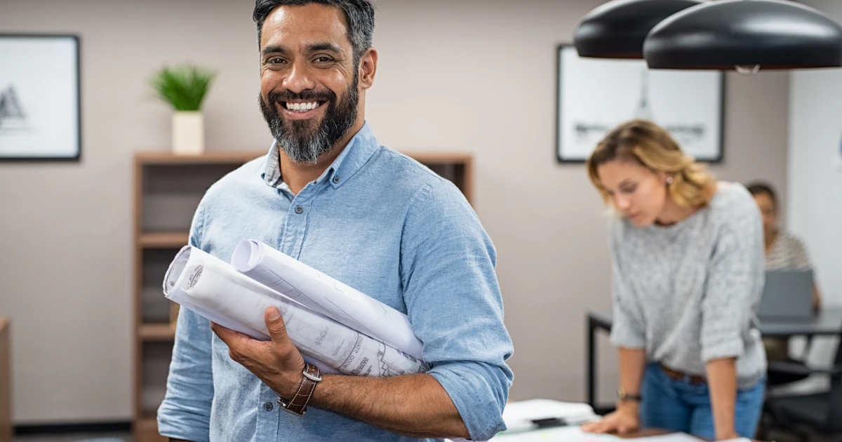 Mature middle eastern contractor holding roll of architectural projects while looking at camera