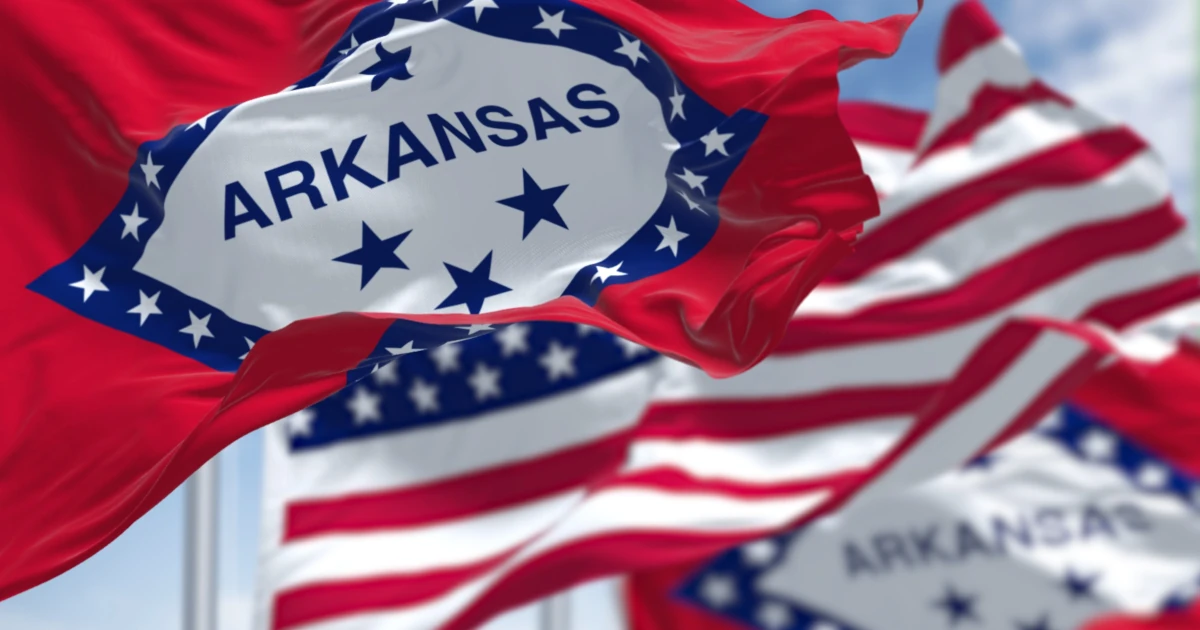 The flags of the Arkansas state and United States waving in the wind