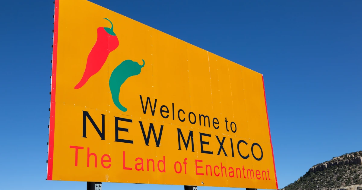 A yellow welcome to New Mexico sign in front of a blue sky