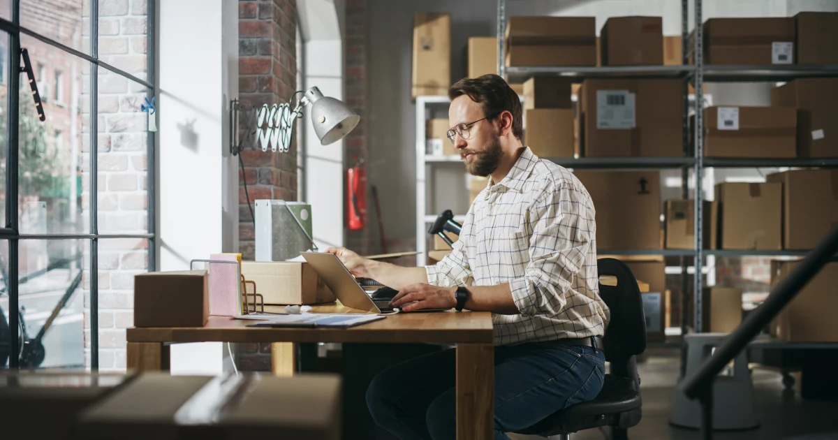 Stylish Young Male Small Business Owner Working on Laptop Computer in Warehouse Facility