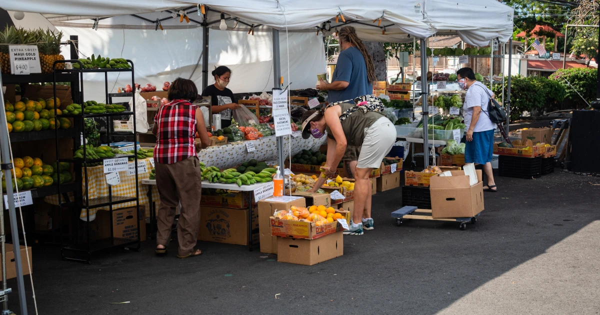 Shoppers choose fresh produce at the white white canopied stall at the Kona Farmer's Market in Hawaii