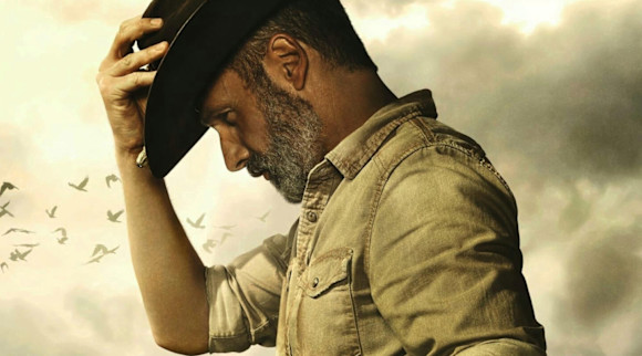 Profile of Rick Grimes with his head down holding the brim of his hat