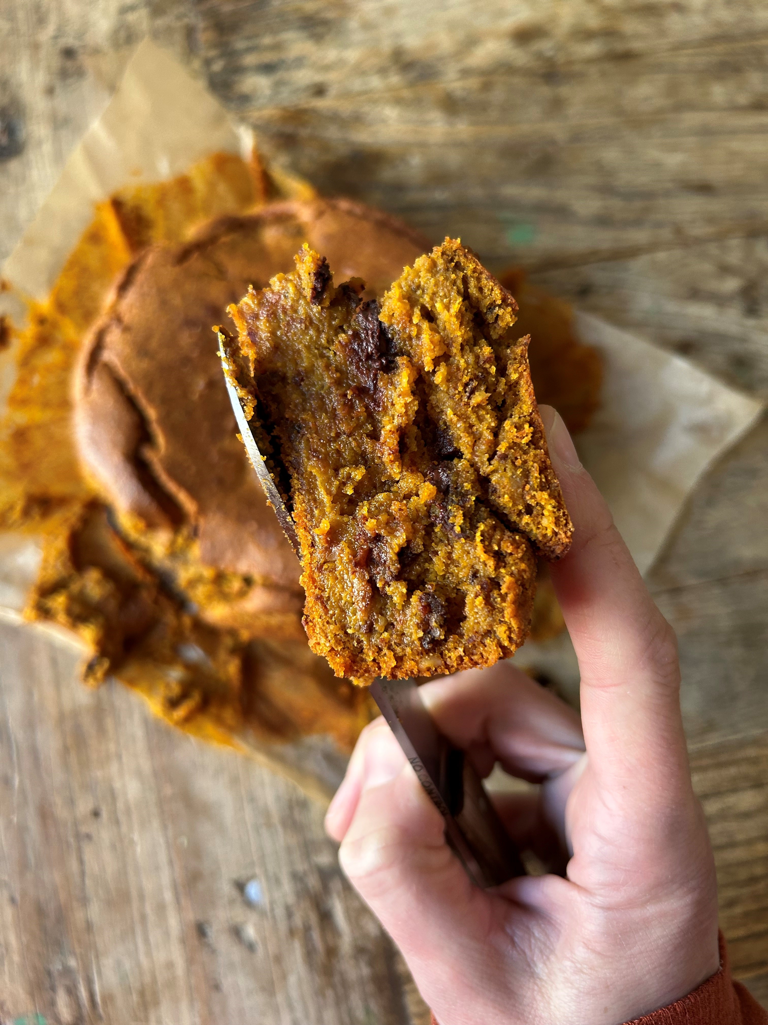Part de blondie à la citrouille et aux pépites de chocolat tenue à la main, texture moelleuse et fondante.