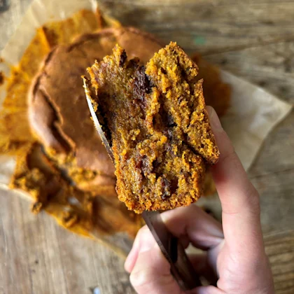 Part de blondie à la citrouille et aux pépites de chocolat tenue à la main, texture moelleuse et fondante.