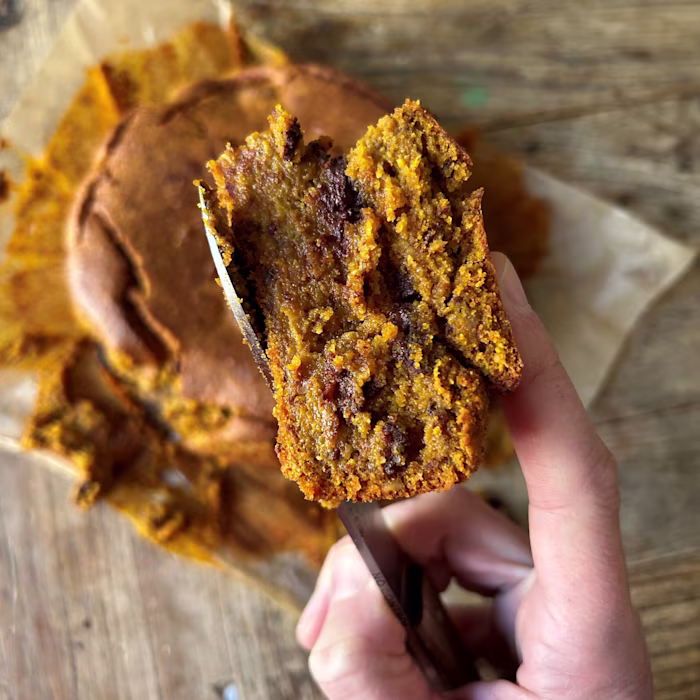 Part de blondie à la citrouille et aux pépites de chocolat tenue à la main, texture moelleuse et fondante.