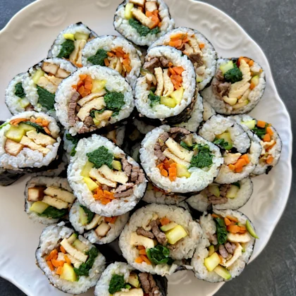 Gimbap coréen roulé dans une feuille de nori, garni de riz assaisonné, légumes sautés, omelette, tofu ou bœuf, coupé en tranches colorées – recette bio NATURALIA