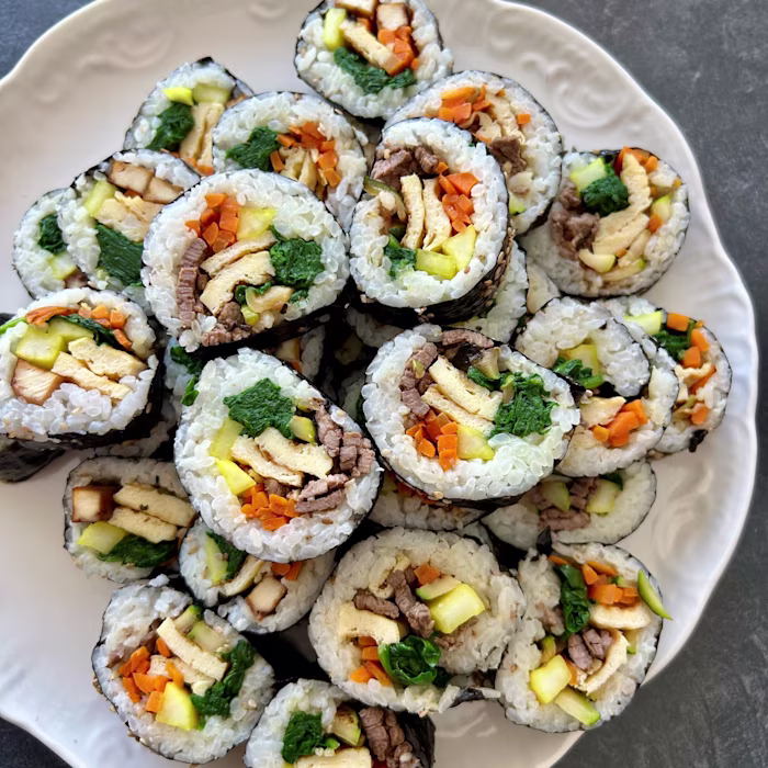 Gimbap coréen roulé dans une feuille de nori, garni de riz assaisonné, légumes sautés, omelette, tofu ou bœuf, coupé en tranches colorées – recette bio NATURALIA