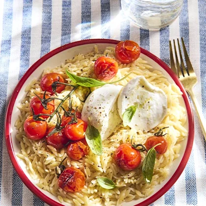 Assiette de pâtes orzo aux tomates et mozzarella sur une nappe rayée