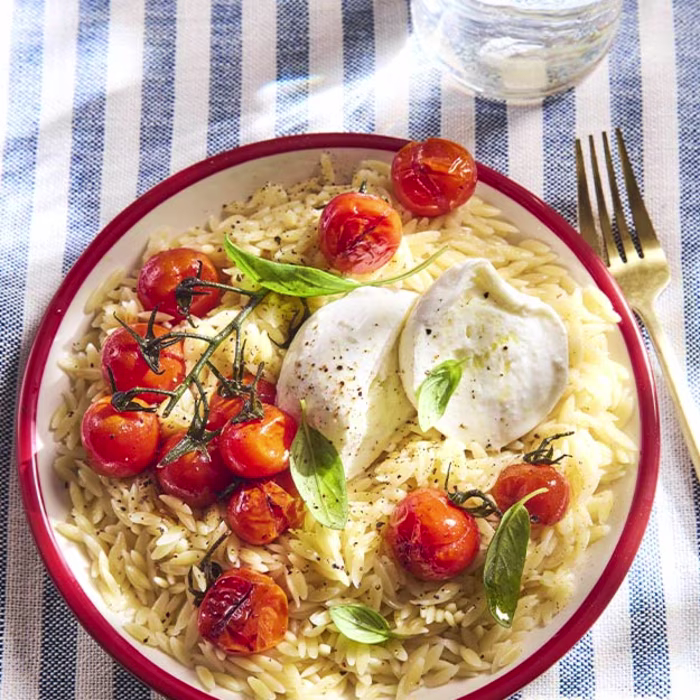 Assiette de pâtes orzo aux tomates et mozzarella sur une nappe rayée
