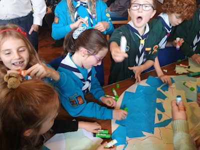 Beavers and Cubs are sticking torn pieces of coloured paper to half a planet. Some of the young people appear to have more glue on their fingers than on the paper. One Cub seems to think the idea is to cover as much paper as possible in glue. He looks rather excited about his glue stick.