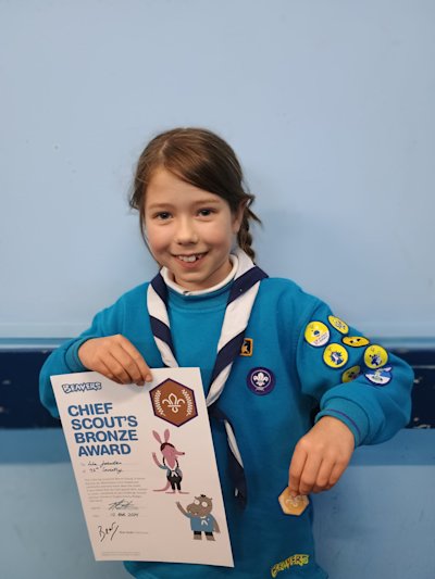 A Beaver holding her hard-earned Bronze award in one hand and her certificate in the other, with a huge smile on her face.