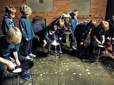 Three Cubs begin the firelighting challenge. One has already got sparks going, but won't be the first to get her cotton wool lit. Their team mates look on and cheer for them.