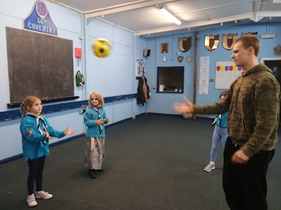 The Beaver girl watches the ball approach her in the air, her hands at the ready, while she waits for the Young Leader who threw the ball to call out Head or Hands.