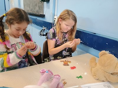 These two Beavers are carefully threading beads onto elastic to make Christmas bracelets. One Beaver is being very kind and making hers for her brother.