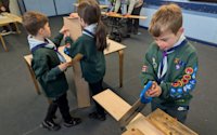 One Cub is cutting a piece of wood, concentration on his face, while two other Cubs sand their pieces.