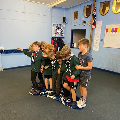 Cubs squished together, standing on a blanket to play the magic carpet game, where the Cubs need to stay standing on the blanket, but flip the blanket over to stand on the other side of the blanket.