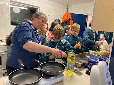 A group of Scouts are in the kitchen, making French toast. One of the Scouts is getting help cracking an egg.