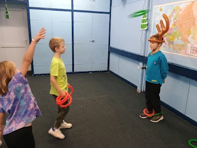 Two Beavers take turns tossing their inflatable rings through the air to land on the reindeer antlers worn by the other Beaver. A green ring is flying through the air towards the antlers. Will it miss?