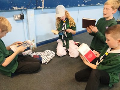 Four Cubs sit grouped around a selection of items they chose from a pile. They're working out where in the world these items come from. One holds a volumatic spacer device for an inhaler, made in England, one holds a book printed in England, and the other two hold books printed in China.