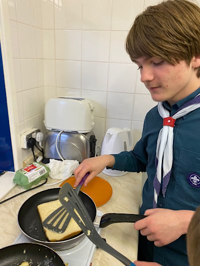 This Scout is paying close attention to his French toast and pressing it lightly in the pan.