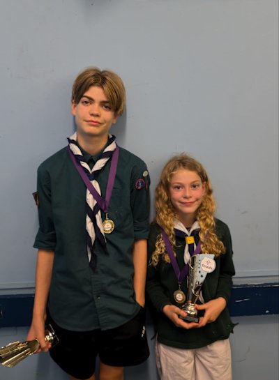 A Scout and his Cub sister stand proudly, displaying their medals and her trophy after they won Scout of the Year and Cub of the Year.