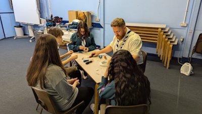 The Scouts are learning to wire a plug from their leader. There are a variety of tools on the table, so they can learn to do it properly.