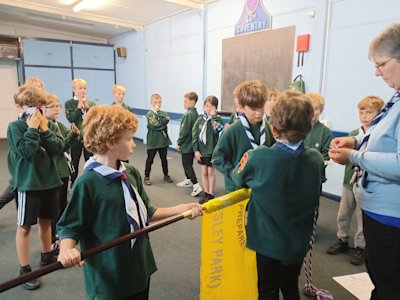 A new Cub has his necker placed on him by his Sixer, while his Seconder holds the Cubs flag he just made his promise on. His Sixer hands him his new membership badges and shakes his hand.