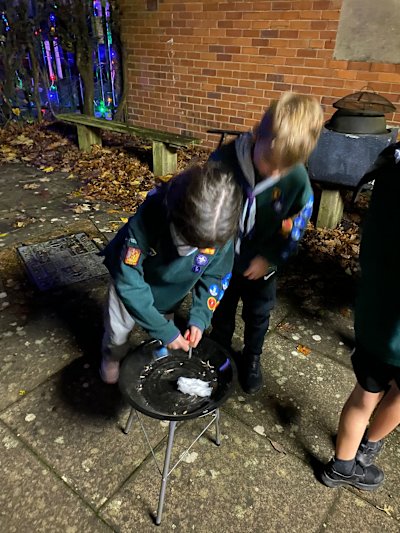 A Cub is trying to get her cotton wool lit in order to win the firelighting competition. Her Sixer is giving her tips from behind her shoulder.