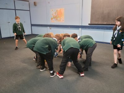 The Cubs are clustered closely together in a circle, their feet wide apart, while they try to get the ball through the legs of someone to get them out.