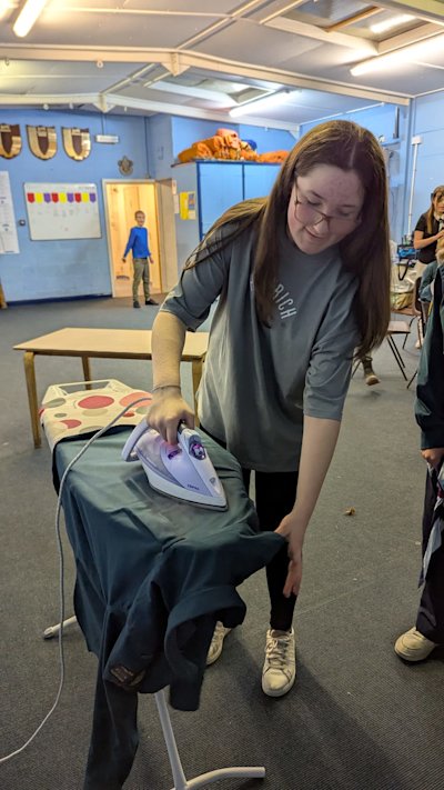 This Scout is carefully ironing her uniform shirt as part of her practical skills.