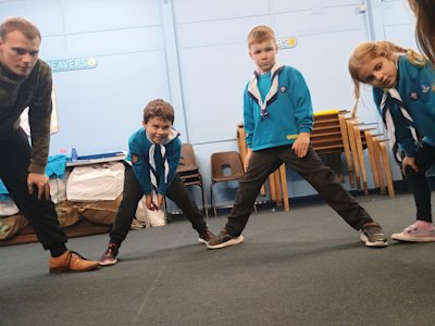 Legs spread wide, a circle of Beavers and their Young Leader wait for the ball to come their way.