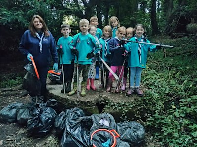 A group of Beavers stand on top of a capped medieval well, an adult volunteer stands next to them, with a pile of bags full of rubbish they've collected in front of them, proud expressions on their faces.