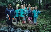 A group of Beavers stand on top of a capped medieval well, an adult volunteer stands next to them, with a pile of bags full of rubbish they've collected in front of them, proud expressions on their faces.