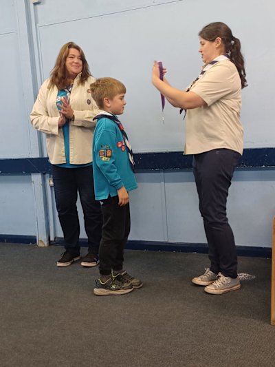 The winner of Beaver of the Year receives his medal from his leader, while his other leader stands by and applauds.