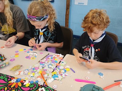 Two Cubs sit decorating paper skulls with foam flowers and felt tip markers. They're taking longer than the others and paying very close attention to their designs.