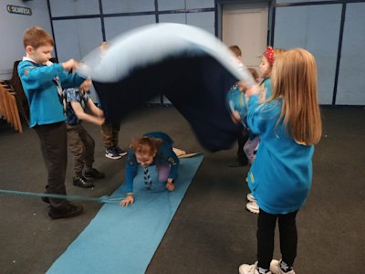 This Beaver has finished her time at Beavers and is moving up to Cubs. As part of the ceremony, she has to crawl under the "river" blanket being waved by the Beaver colony, holding onto a rope pulled by a Cub waiting to receive her into the Pack.